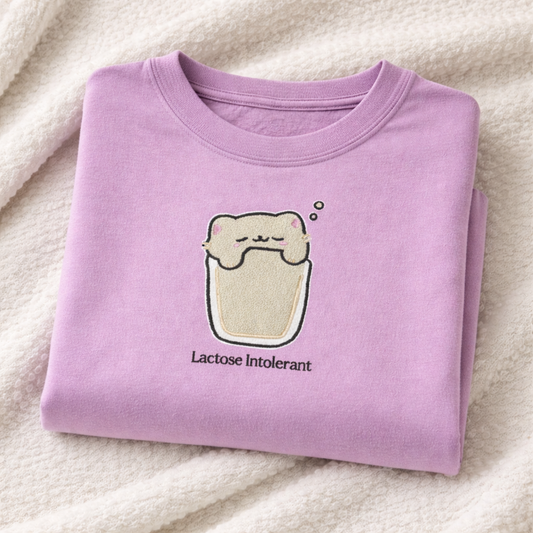 Folded orchid t-shirt with a cartoon embroidered design and text on a white fabric background