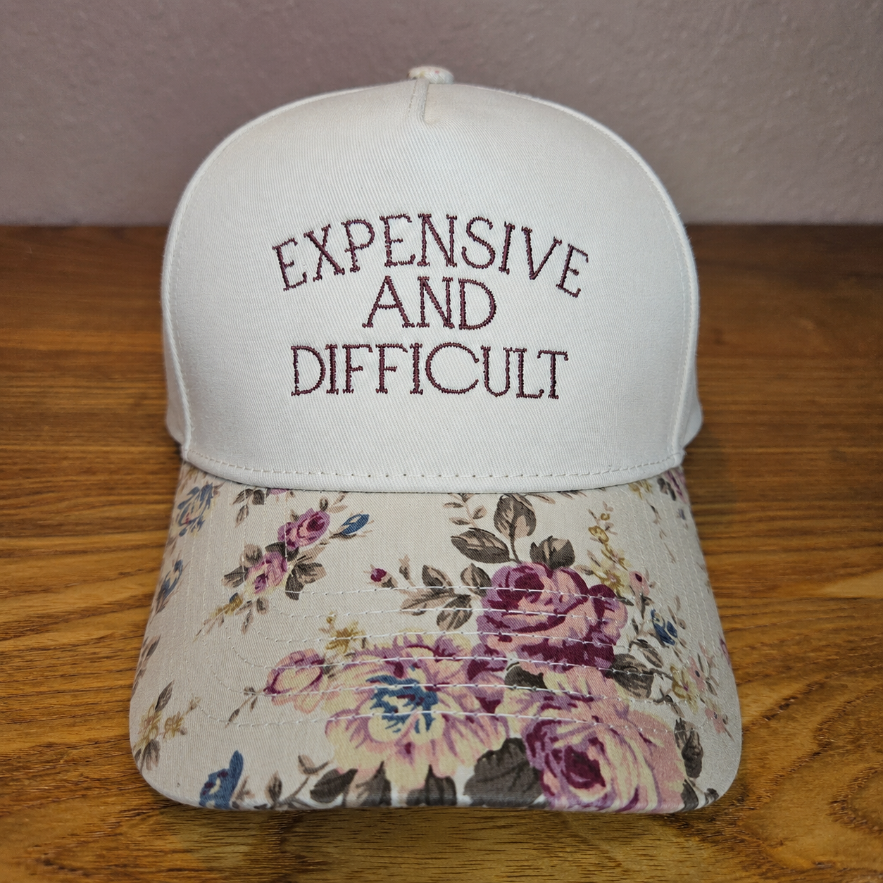 White cap with floral brim and embroidered text on a wooden surface