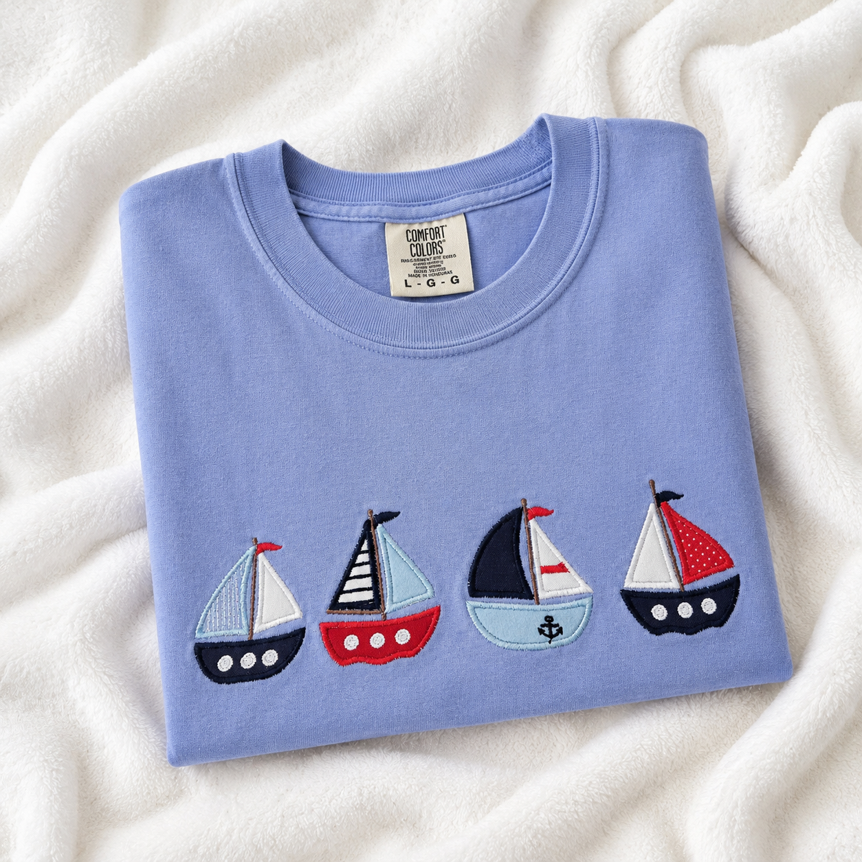 Folded light blue t-shirt with sailboat designs on a white textured surface