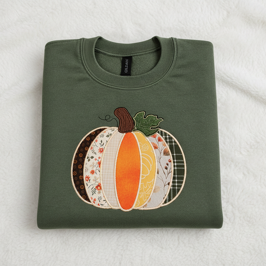 A folded military green Gildan sweatshirt featuring a large, colorful patchwork pumpkin applique on the front, set against a plain white background.
