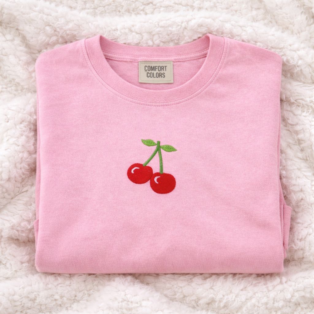 Light pink sweatshirt with cherry design on a fluffy white surface