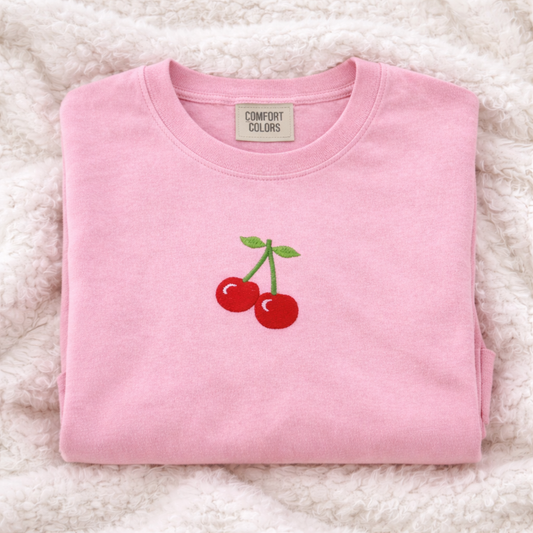 Light pink sweatshirt with cherry design on a fluffy white surface