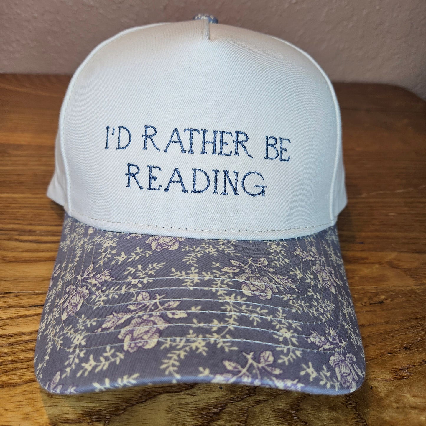 Floral-patterned hat with 'I'd Rather Be Reading' text on a wooden surface