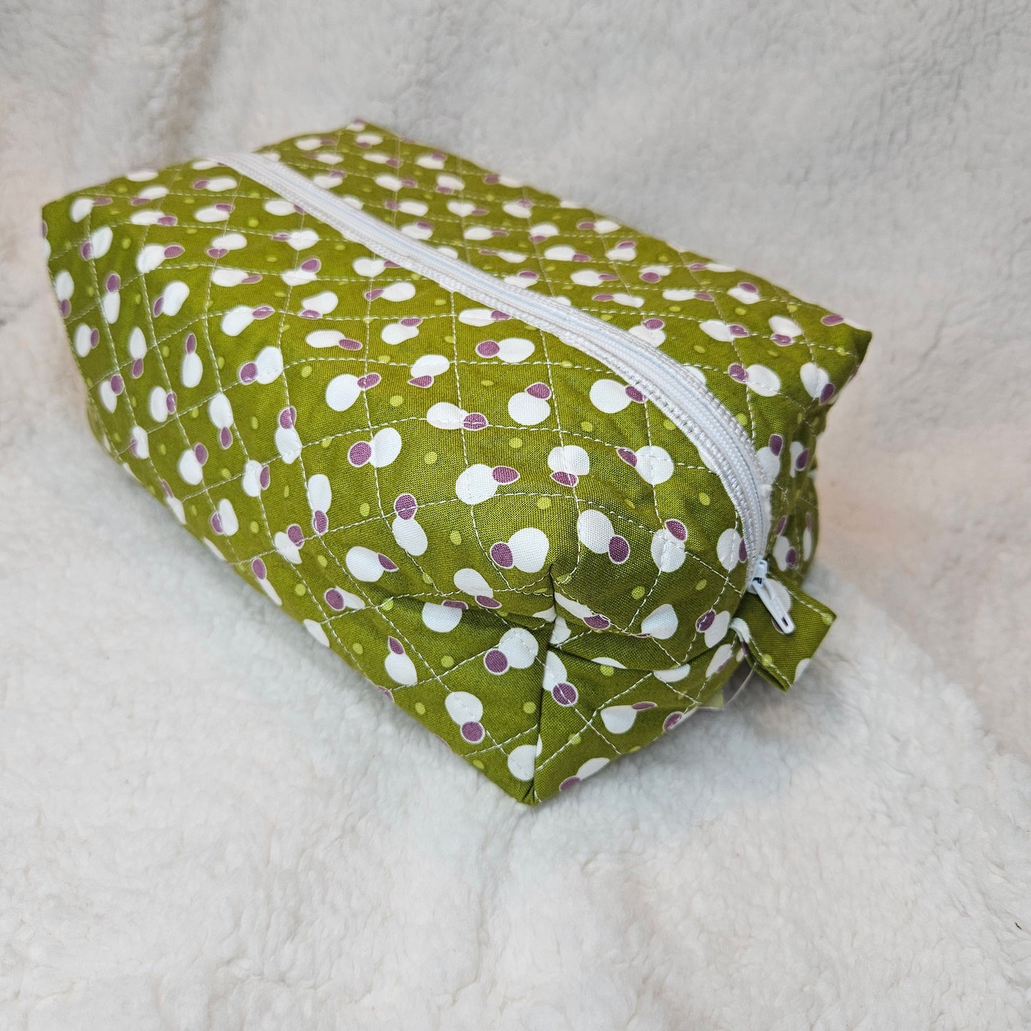 Green fabric pouch with white zipper on a light gray background
