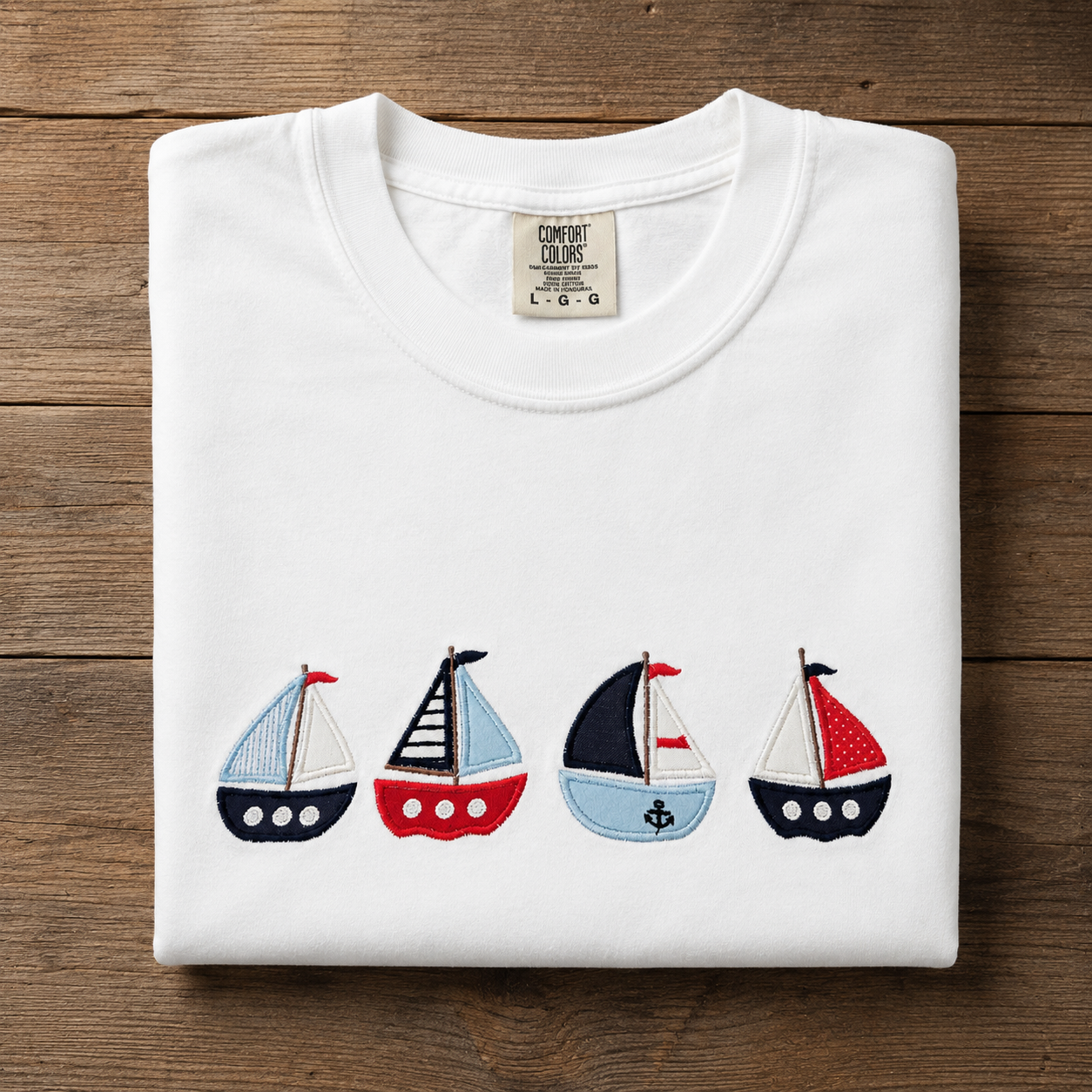 Folded white t-shirt with sailboat designs on a wooden surface