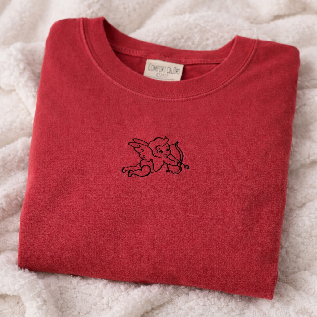 Folded crimson t-shirt with a black embroidered design on a white fluffy surface