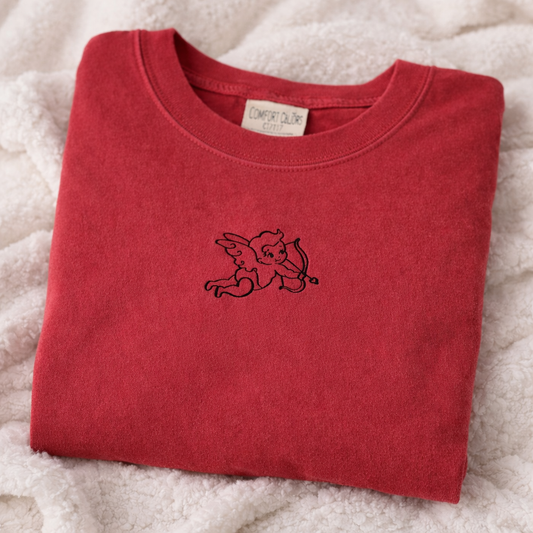 Folded crimson t-shirt with a black embroidered design on a white fluffy surface