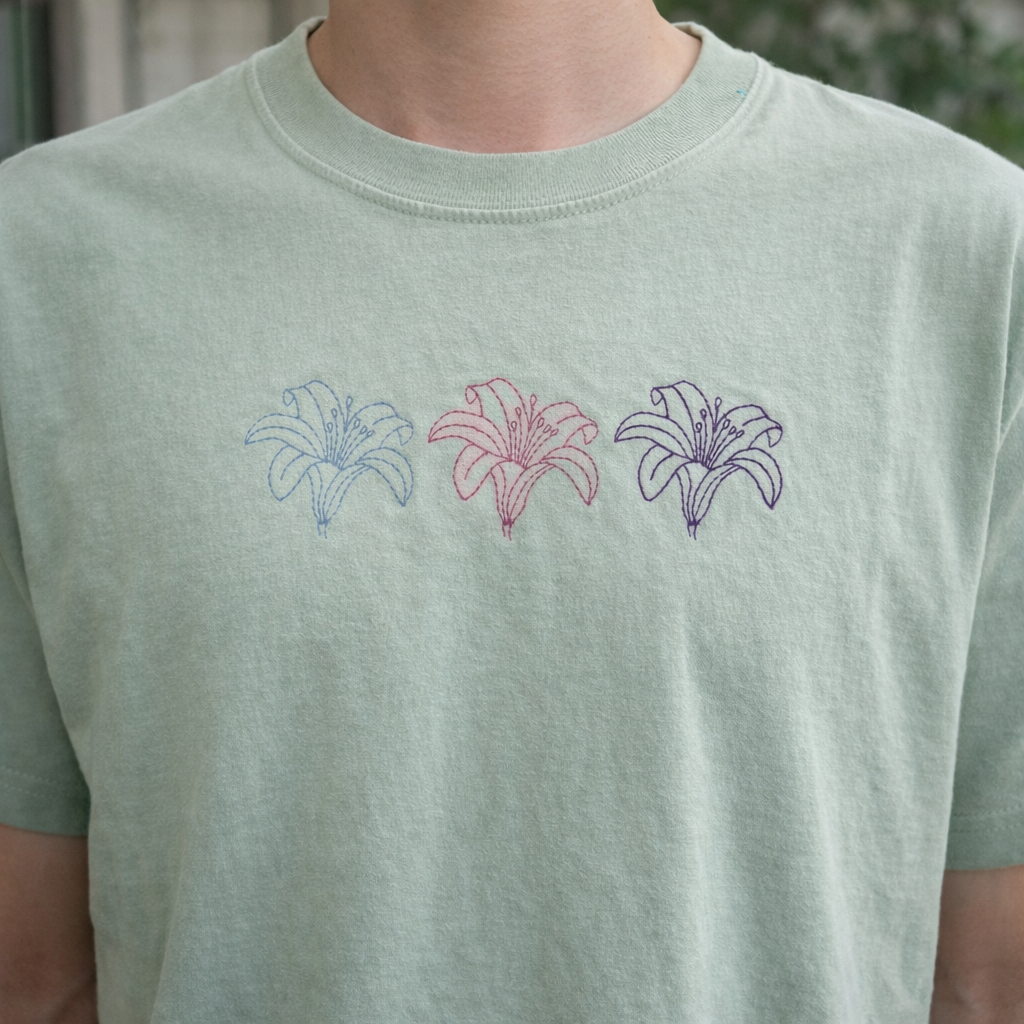 Sage t-shirt with embroidered floral designs on a blurred background