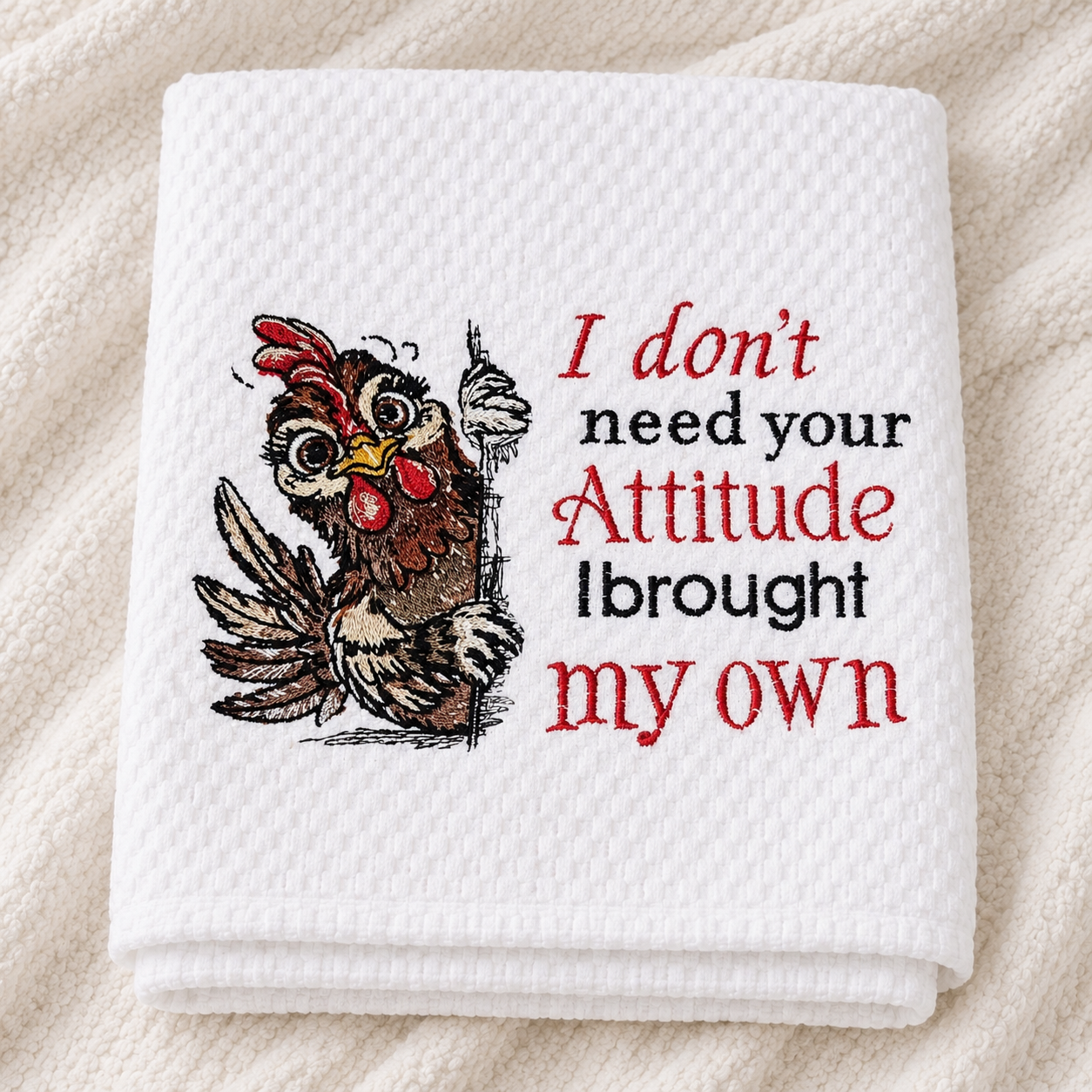Folded white towel with a rooster embroidered design and text on a beige fabric background