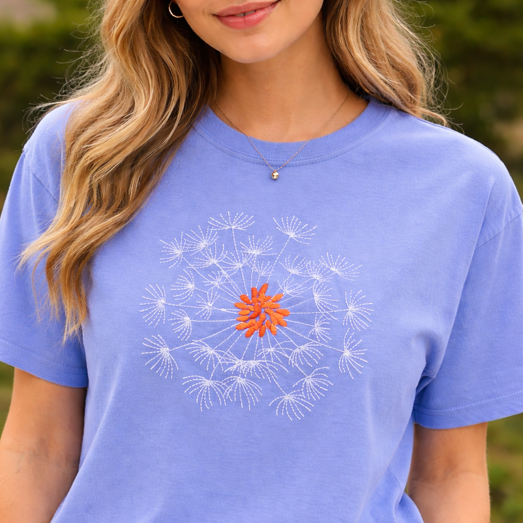 Person wearing a hydrangea t-shirt with a dandelion design, outdoors.