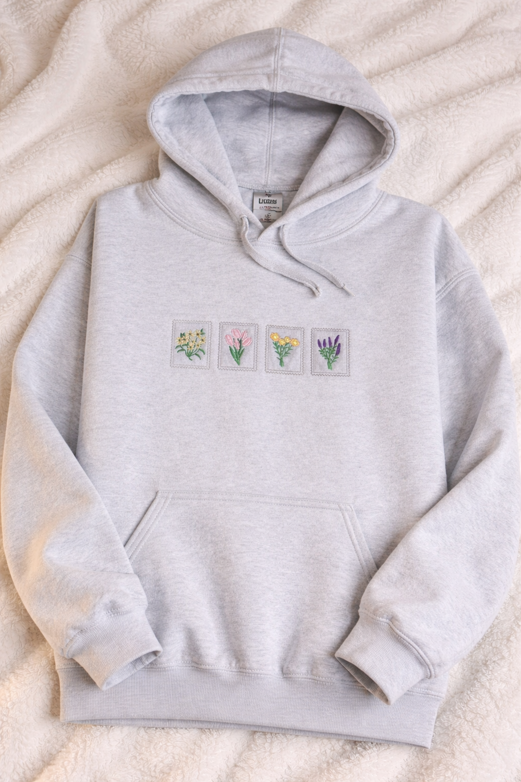 Ash hoodie with small floral embroidered designs on a beige surface