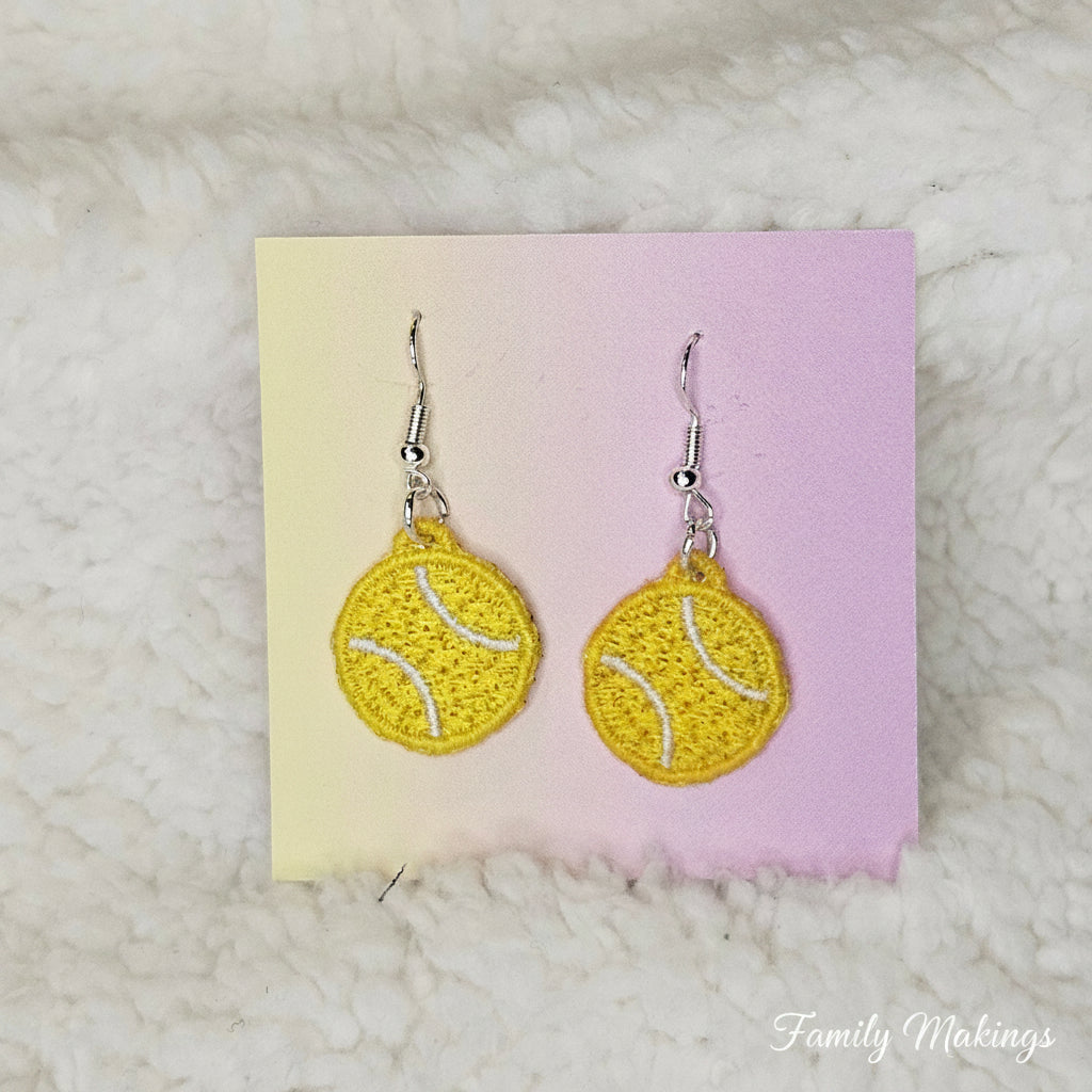 Yellow tennis ball earrings on a pink and yellow card with a white textured background