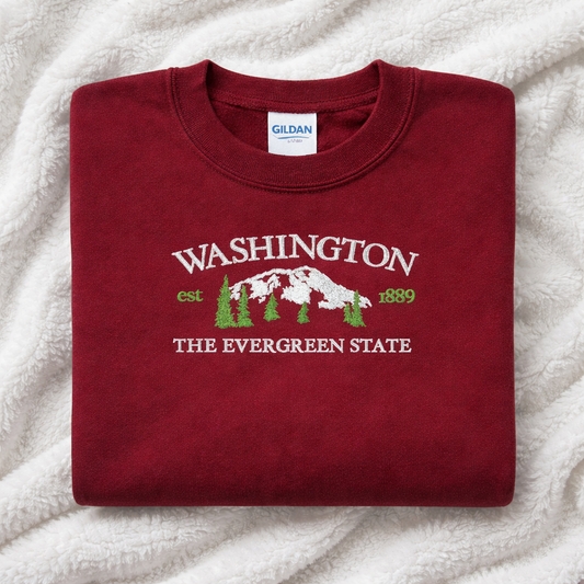Folded maroon sweatshirt with 'Washington The Evergreen State' text and design on a white blanket background