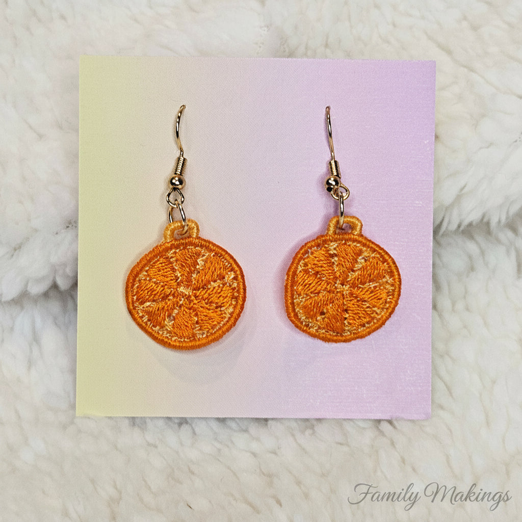 Embroidered orange slice earrings with gold posts on a card
