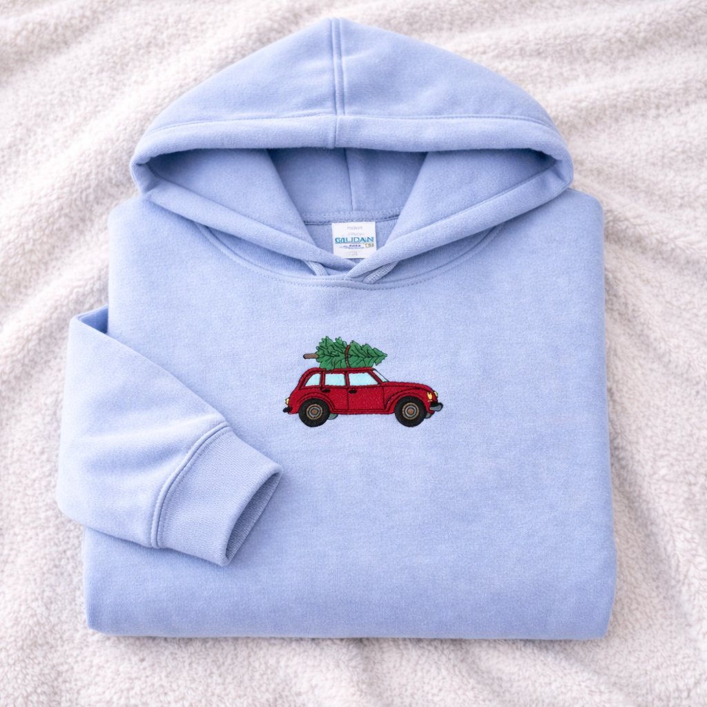 Light blue hoodie with a red car and Christmas tree design on a white blanket