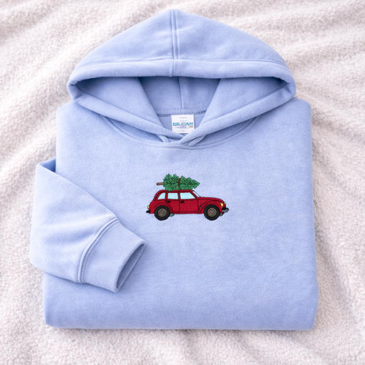 Light blue hoodie with a red car and Christmas tree design on a white blanket