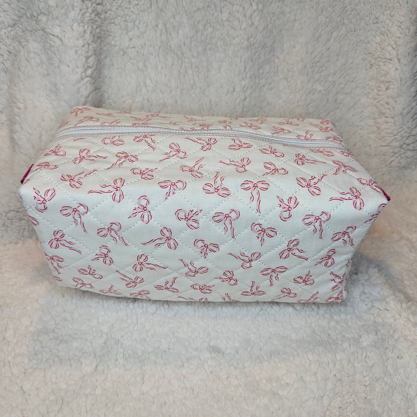 Small rectangular pouch with pink bow pattern on a textured beige surface