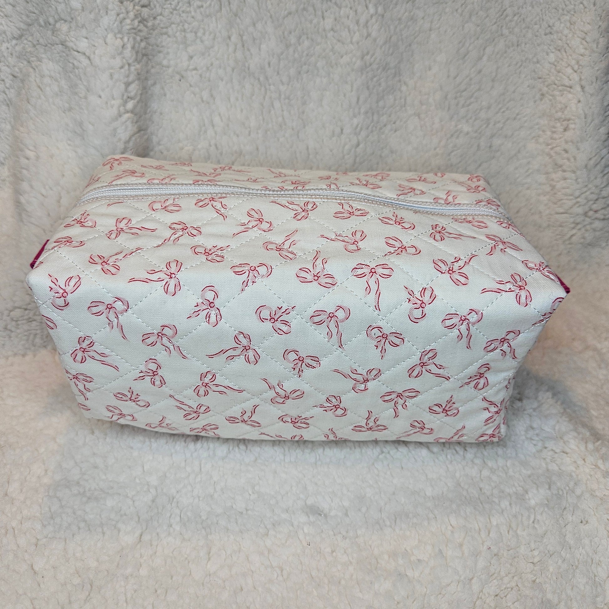 Small rectangular pouch with pink bow pattern on a textured beige surface