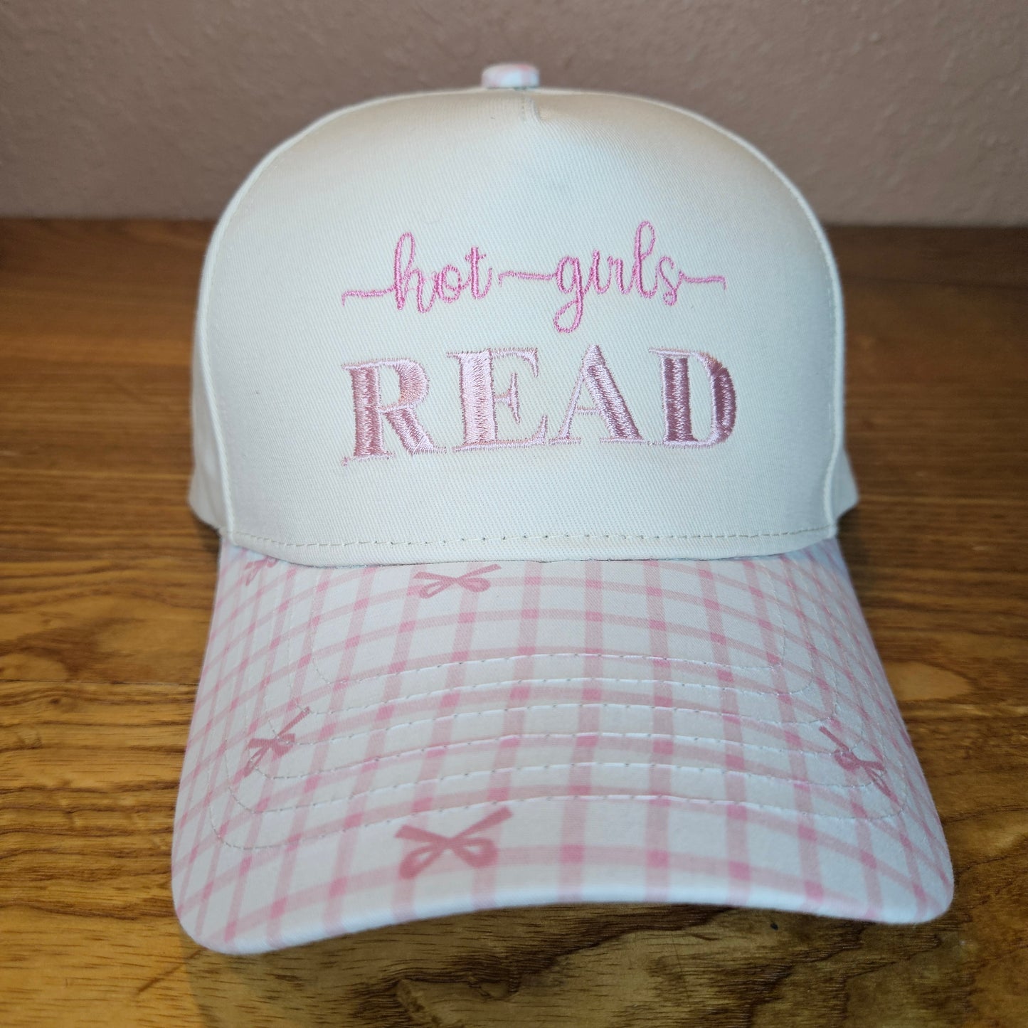 White hat with pink plaid fabric and embroidered text on a wooden surface