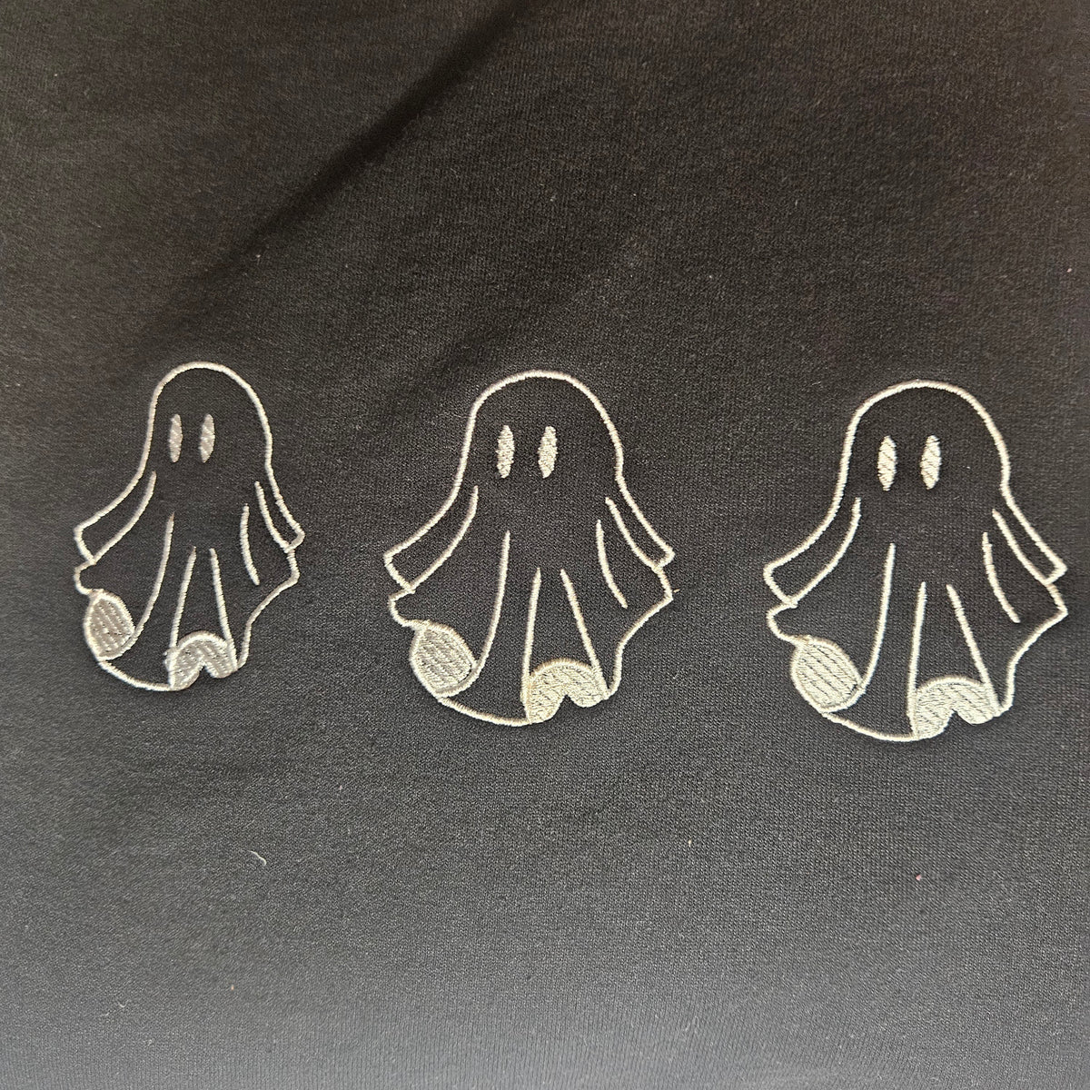 Three small embroidered ghost embroidered on black fabric background.