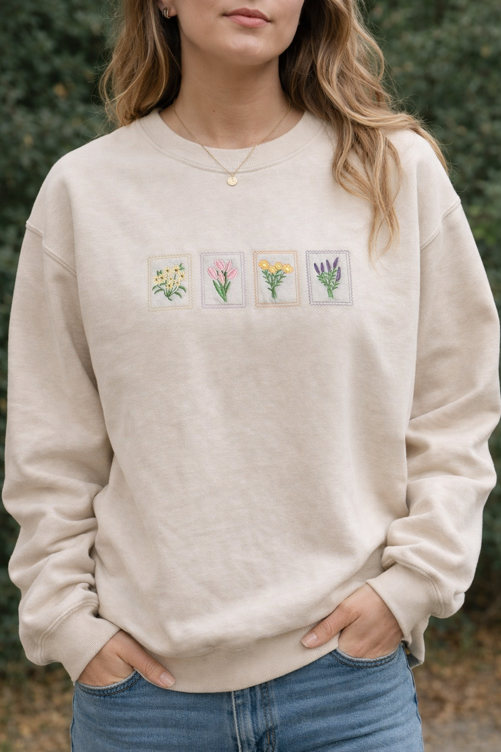Person wearing a sand sweatshirt with floral embroidery, standing outdoors.