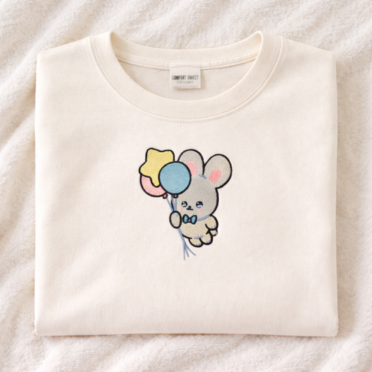 Ivory t-shirt with a cartoon bunny design holding balloons on a white background