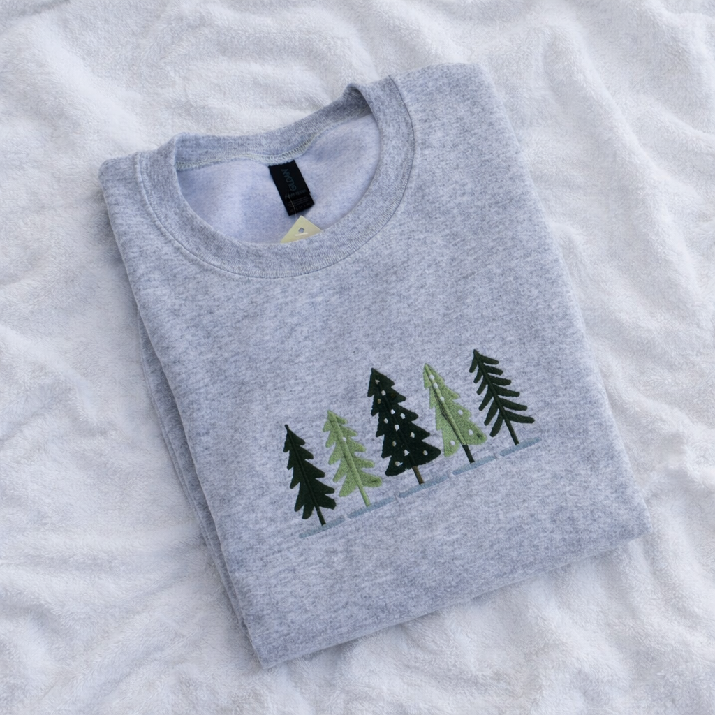 Folded ash gray sweatshirt with green tree designs on a white textured background