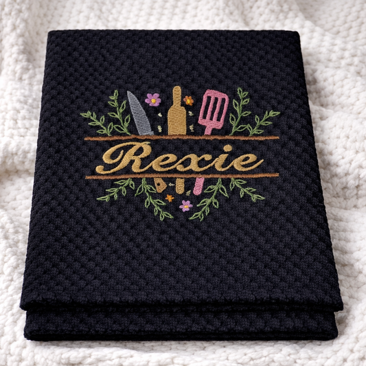 Black towel with embroidered design and 'Rexie' text on a white textured background