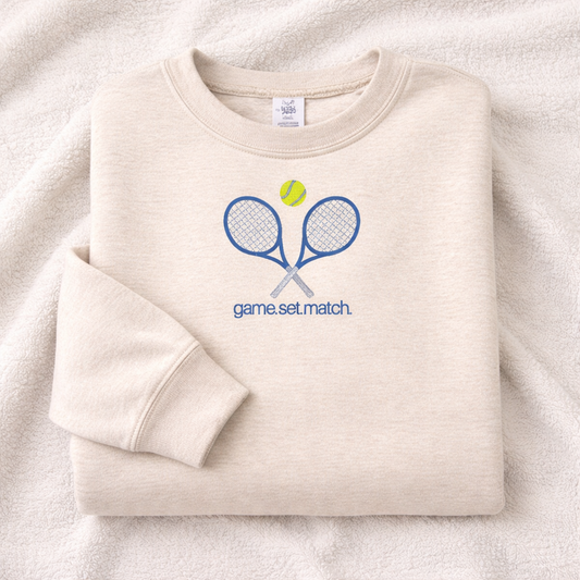 Folded sand sweatshirt with tennis-themed design on a white background