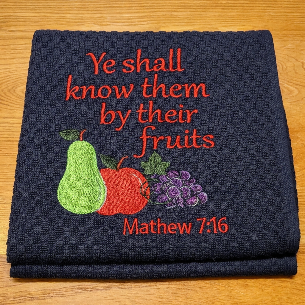 Folded towel with embroidered fruits and text on a wooden surface