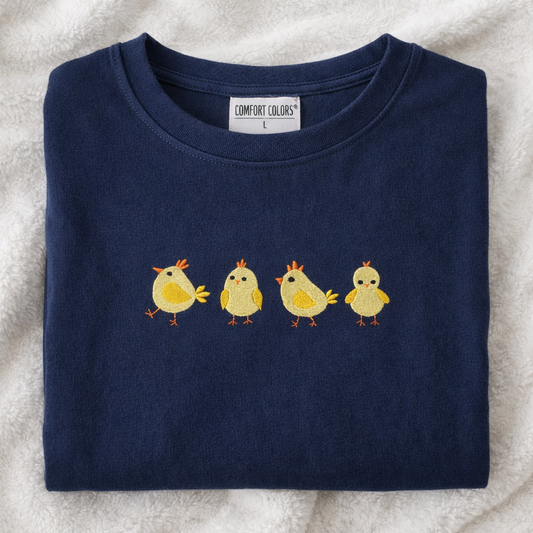 Folded navy t-shirt with yellow chick design on a textured surface