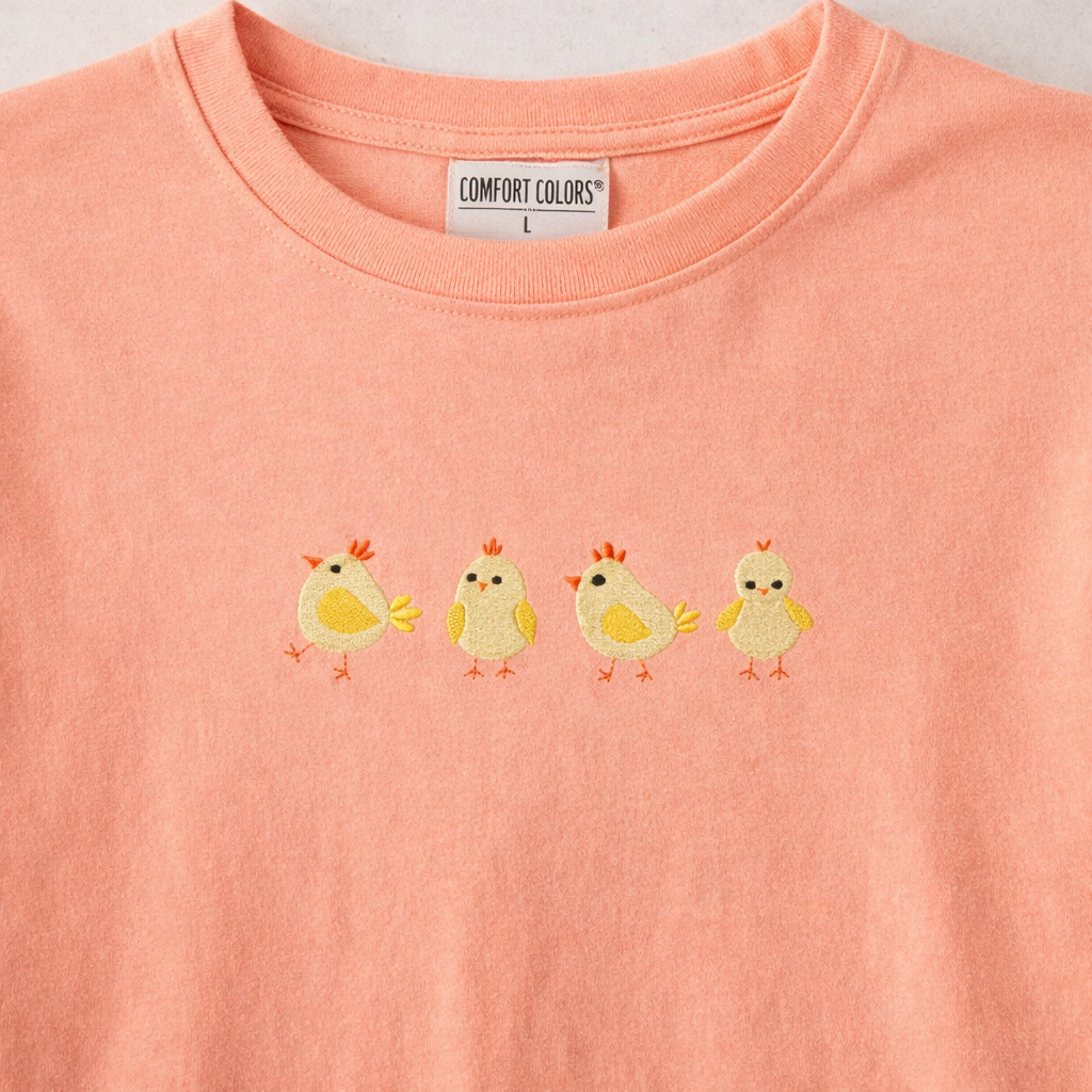 Peachy t-shirt with four embroidered yellow chicks on a plain background