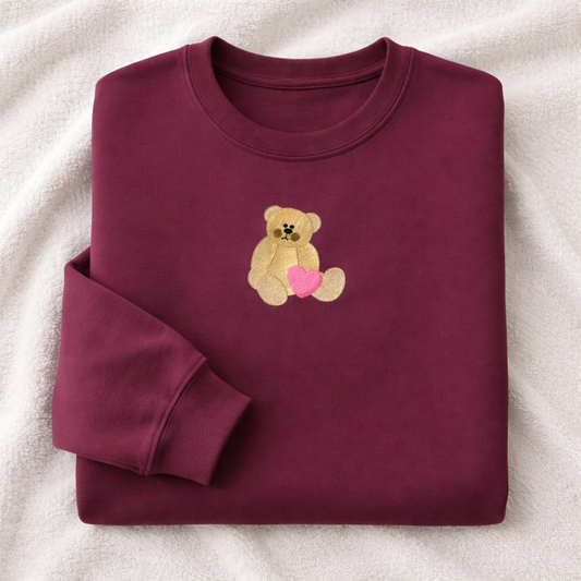 Folded maroon sweatshirt with a teddy bear and heart design on a white background