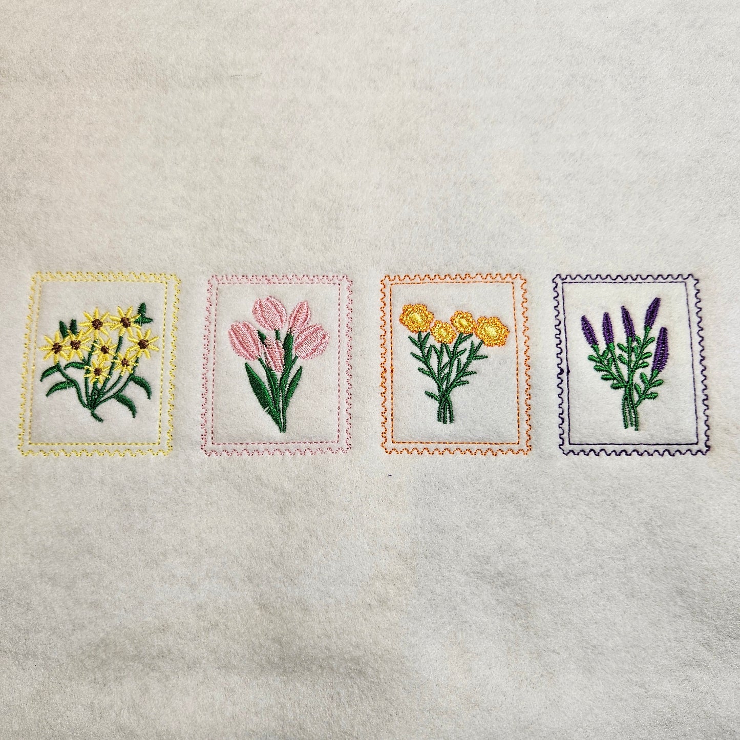 Four embroidered squares with floral designs on a textured fabric background