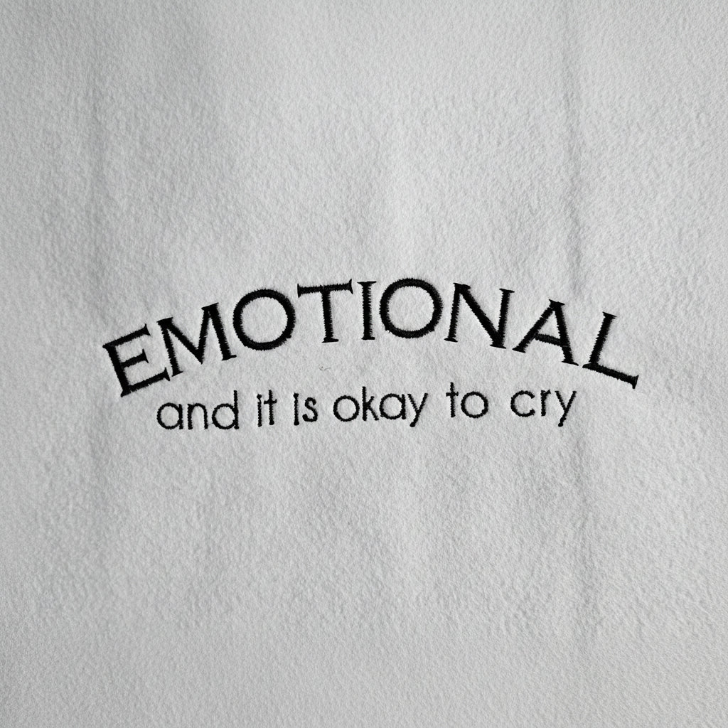 Embroidered text 'EMOTIONAL and it is okay to cry' on a textured white background