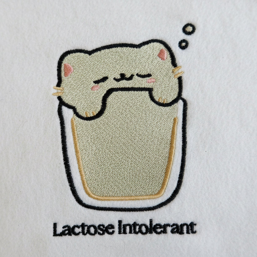 Embroidered design of a cat in a glass with 'Lactose Intolerant' text on a white background