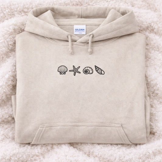 Sand hoodie with shell designs on a fluffy white surface