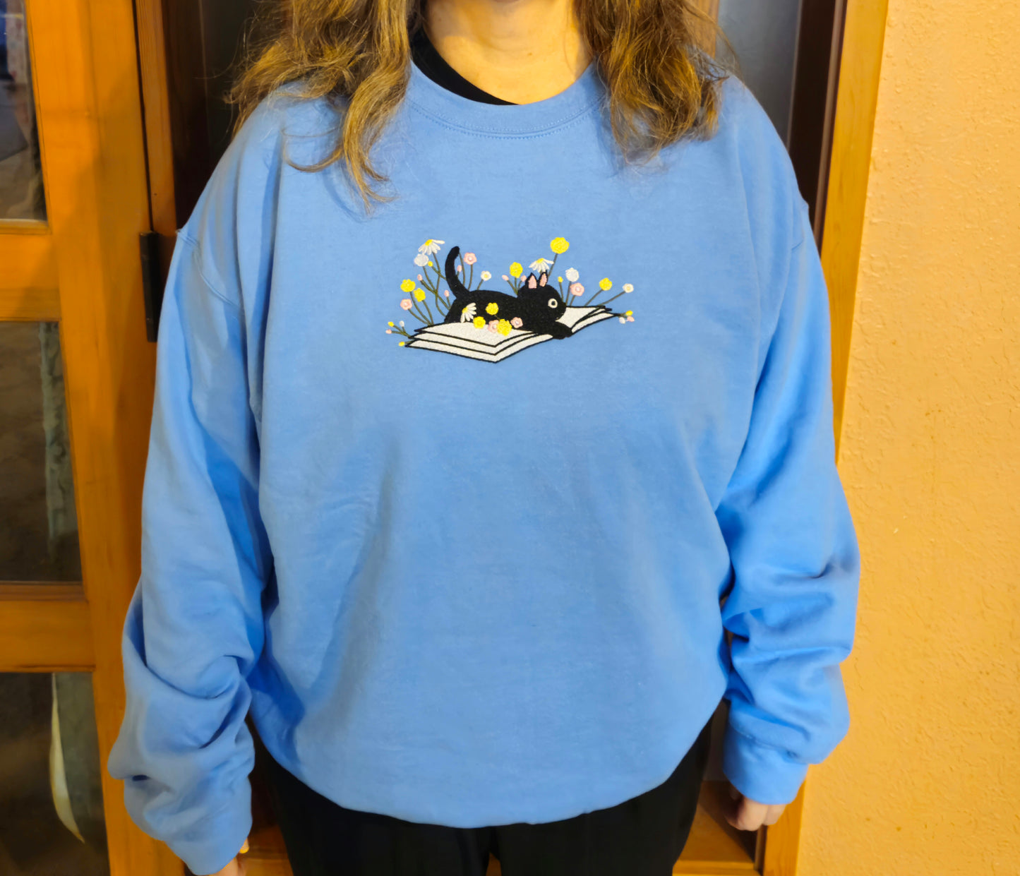 Person wearing the carolina blue sweatshirt with a black cat and book design.