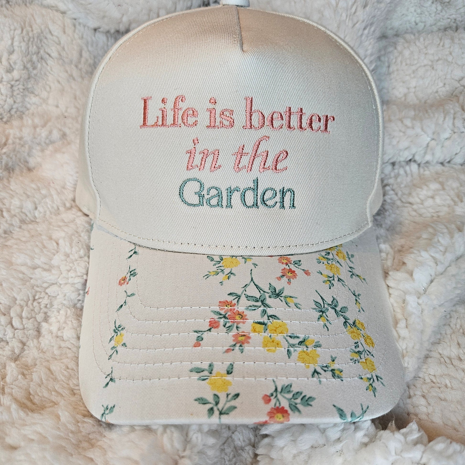 Cap with 'Life is better in the Garden' text and floral design on a soft fabric background