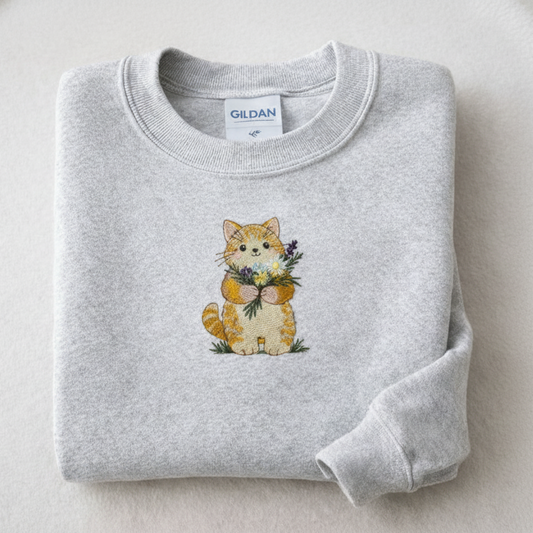 Folded ash sweatshirt with a cat holding flowers design on a light background