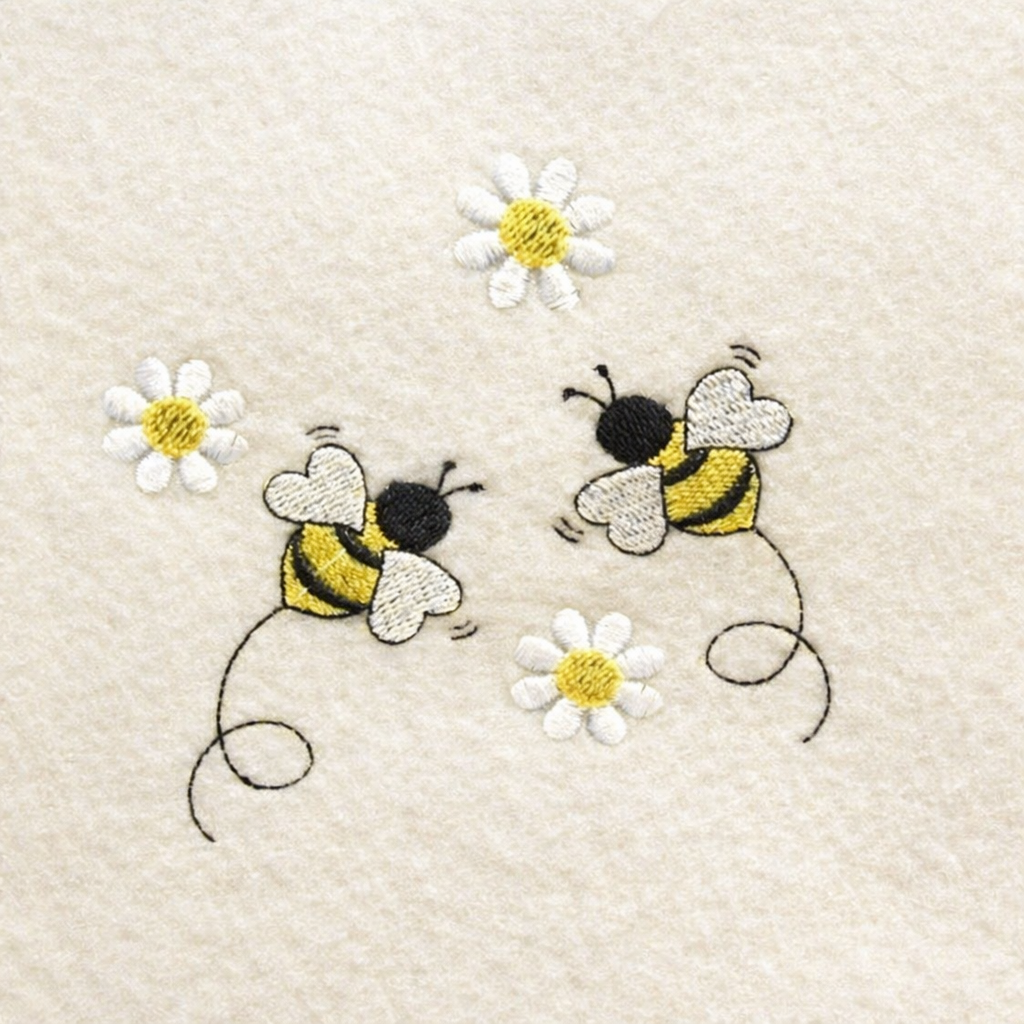 Embroidered design of two bees and three daisies on a beige fabric background