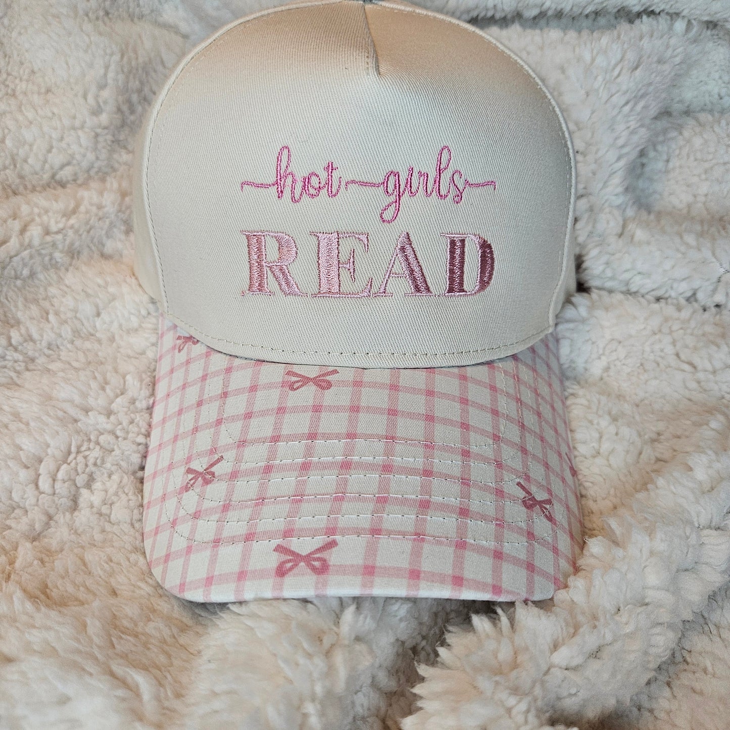 Decorative hat with 'hot girls read' text and a checkered pattern on a soft surface.