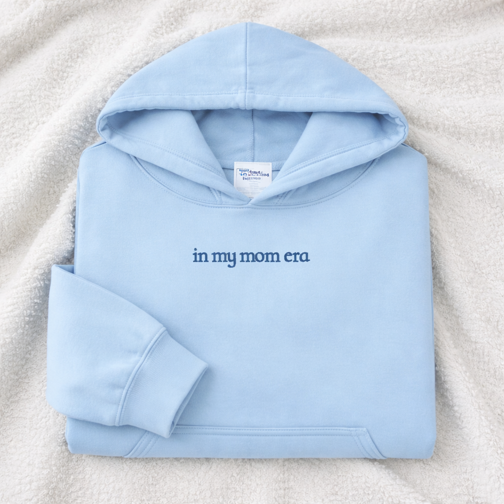 Light blue hoodie with 'in my mom era' embroidered text on a textured surface