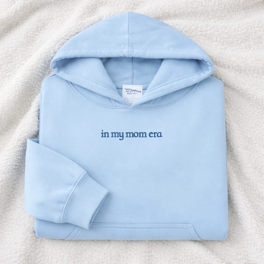 Light blue hoodie with 'in my mom era' embroidered text on a textured surface