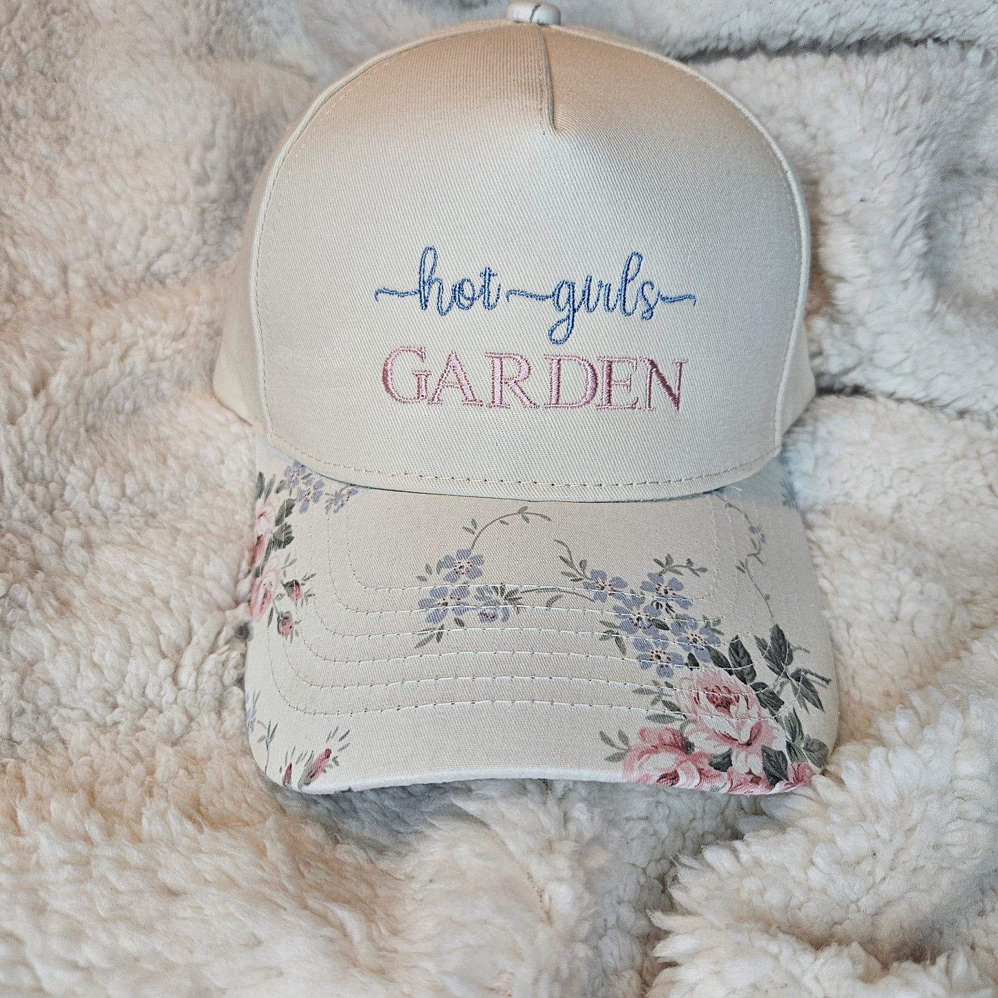 Floral-patterned hat with embroidered text on a fluffy white surface