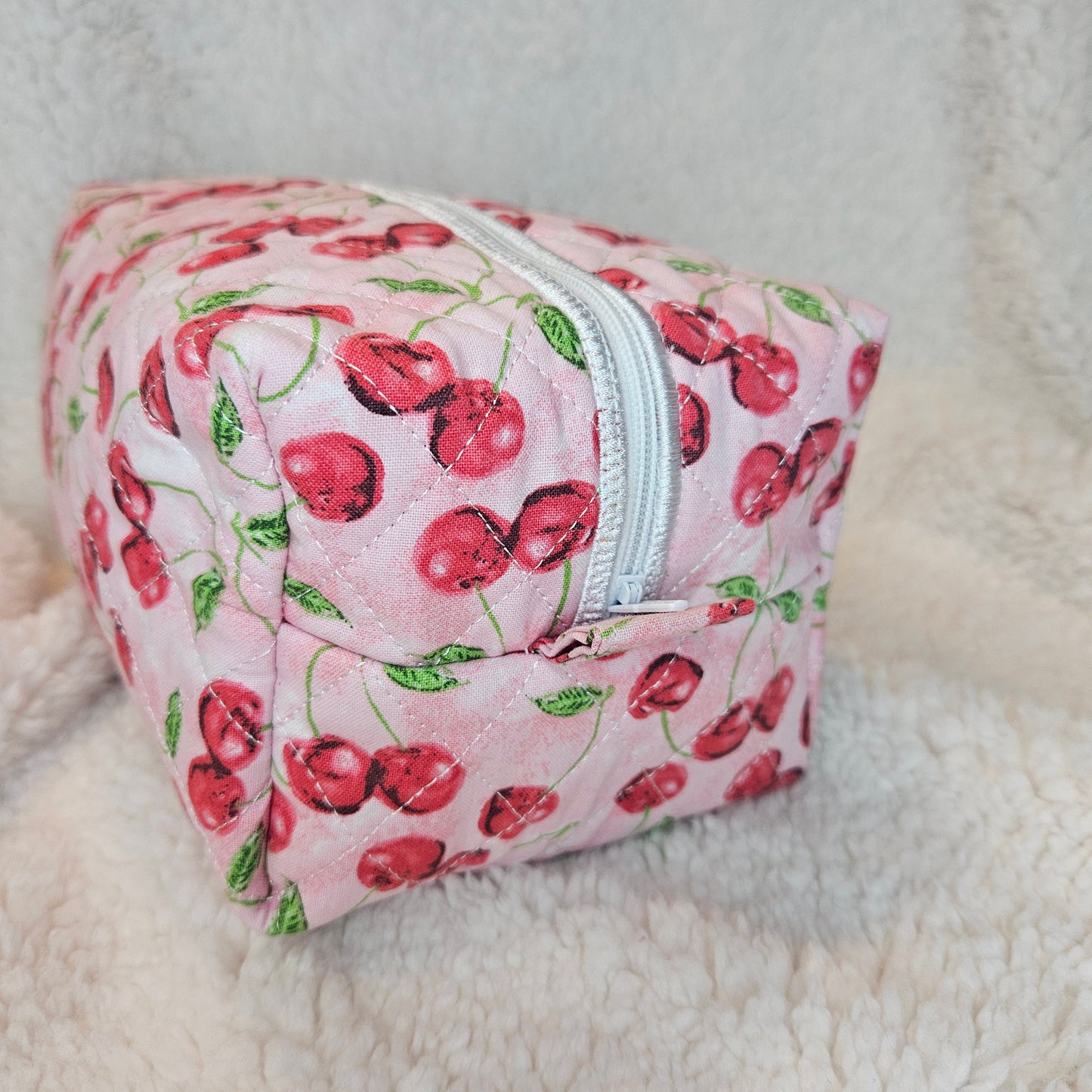 Pink fabric pouch with cherry pattern on a white blanket