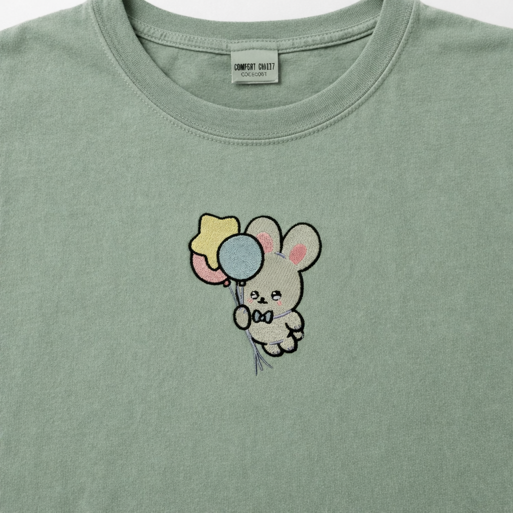 Sage t-shirt with a cartoon bunny holding balloons design on a plain background
