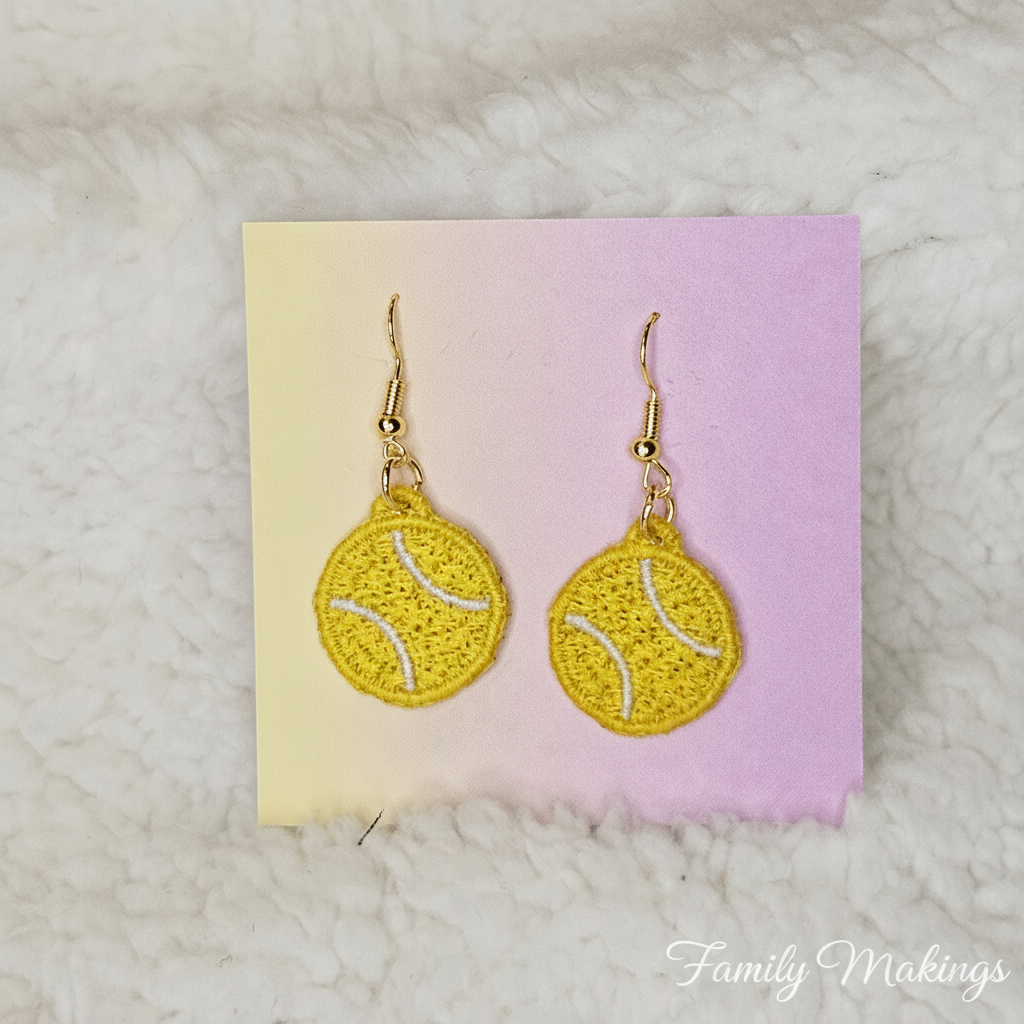 Yellow earrings with tennis ball design on a pink and yellow card, placed on a textured surface.