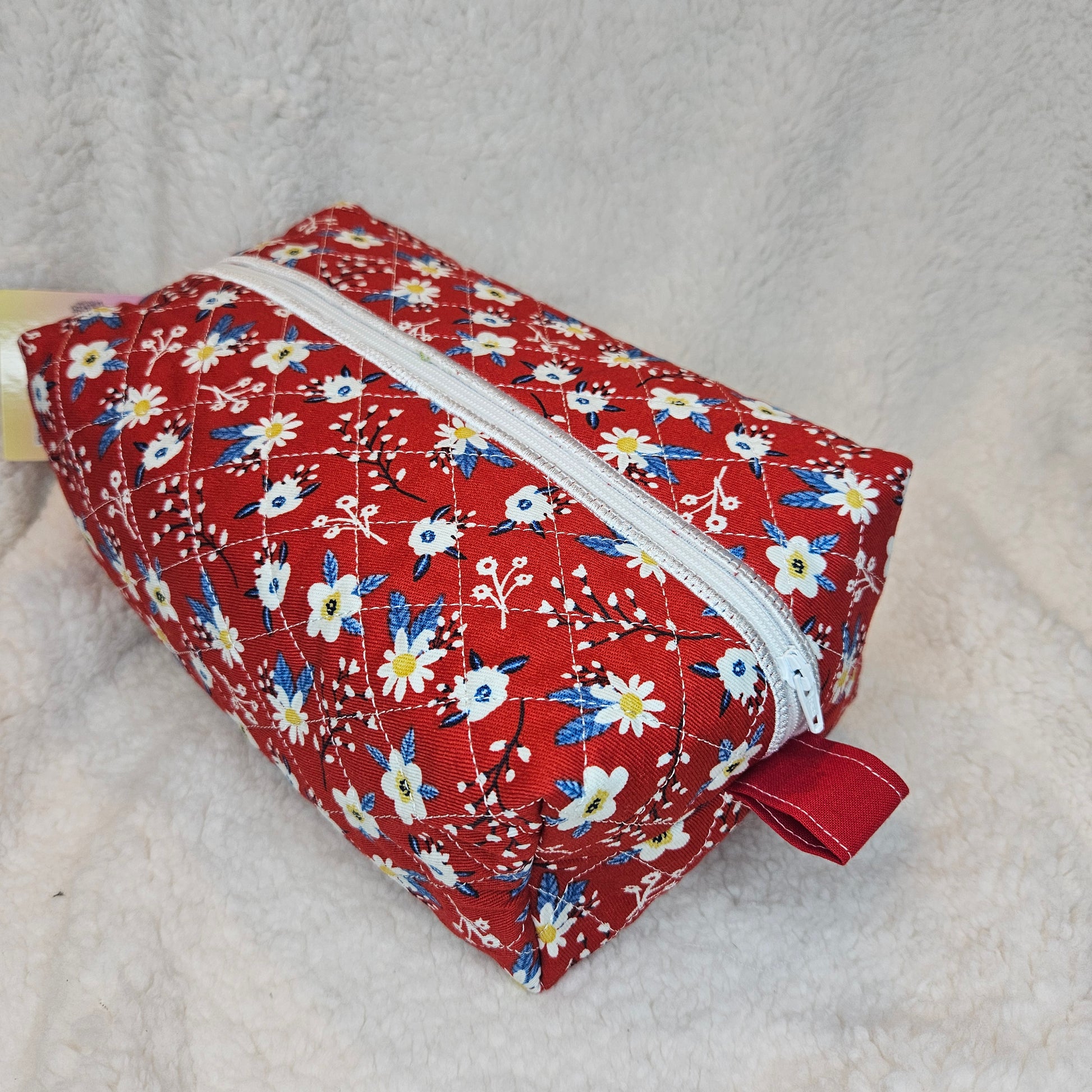 Red floral-patterned fabric bag with a white zipper on a textured surface