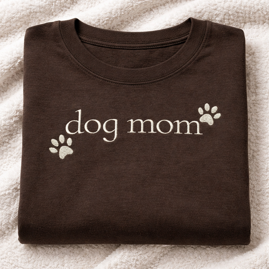 Folded espresso t-shirt with 'dog mom' embroidered text on a textured surface